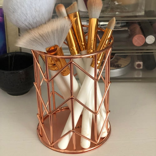 Rose gold makeup brush holder with brushes on a vanity table