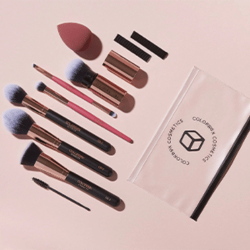 Makeup brushes and tools on a pink background with a clear pouch featuring a logo.